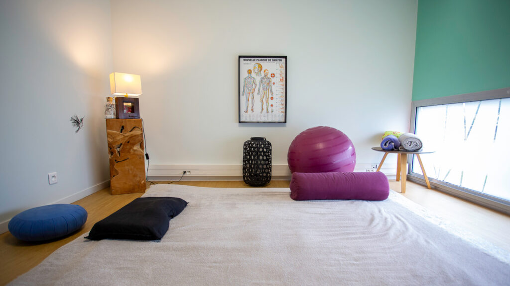 photo en plan large du cabinet d'Alexandra Frelon situé au Poiré-sur-Vie, un tapis au sol, un ballon physio, des serviettes de toilettes, le tout dans une ambiance zen.